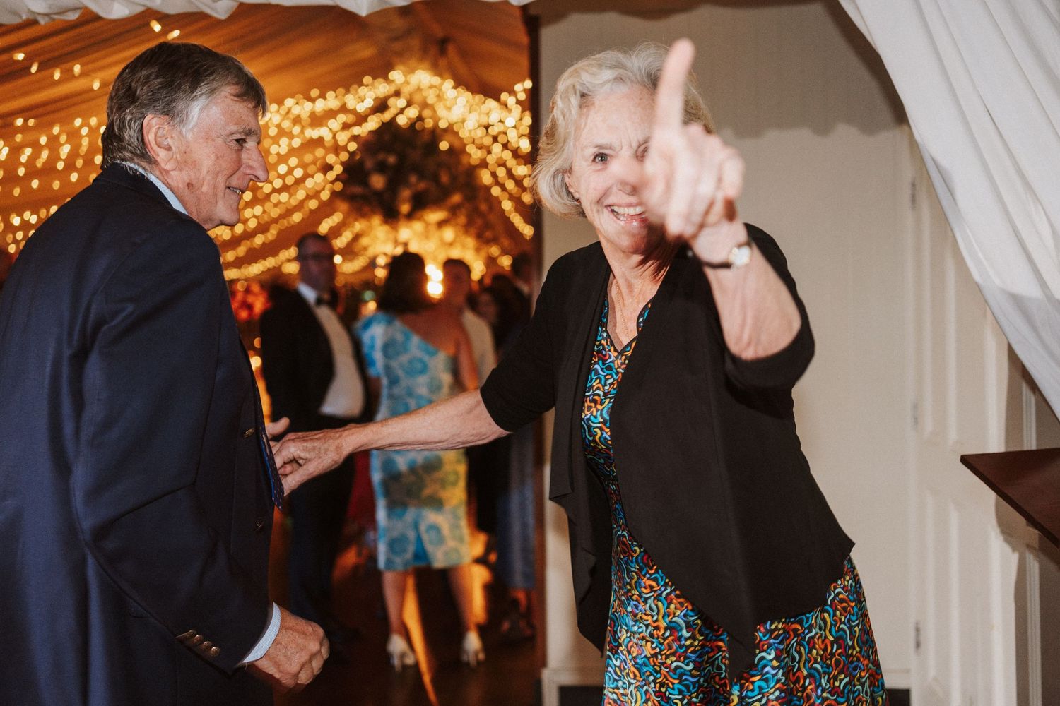 Wedding guests enjoying themselves on a dance floor decorated with warm string lights and white fabric.