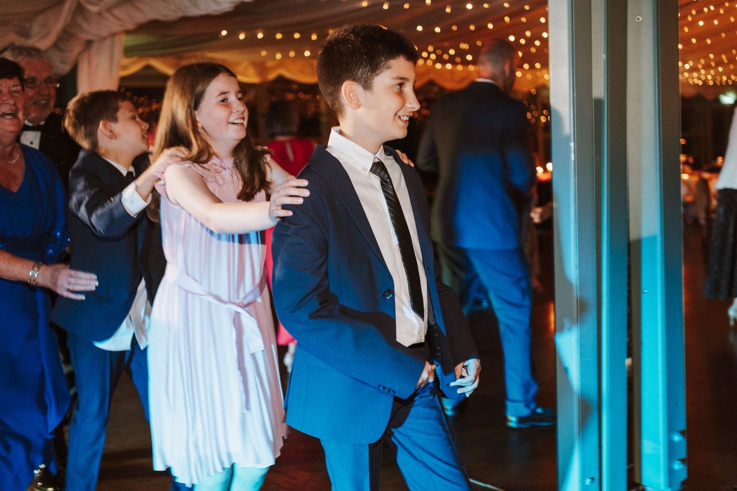 Guests dancing at an evening wedding reception under elegant tent draping and string lighting.
