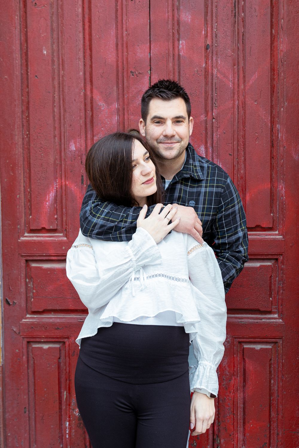 A couple poses playfully against a weathered red door background during a photo session.