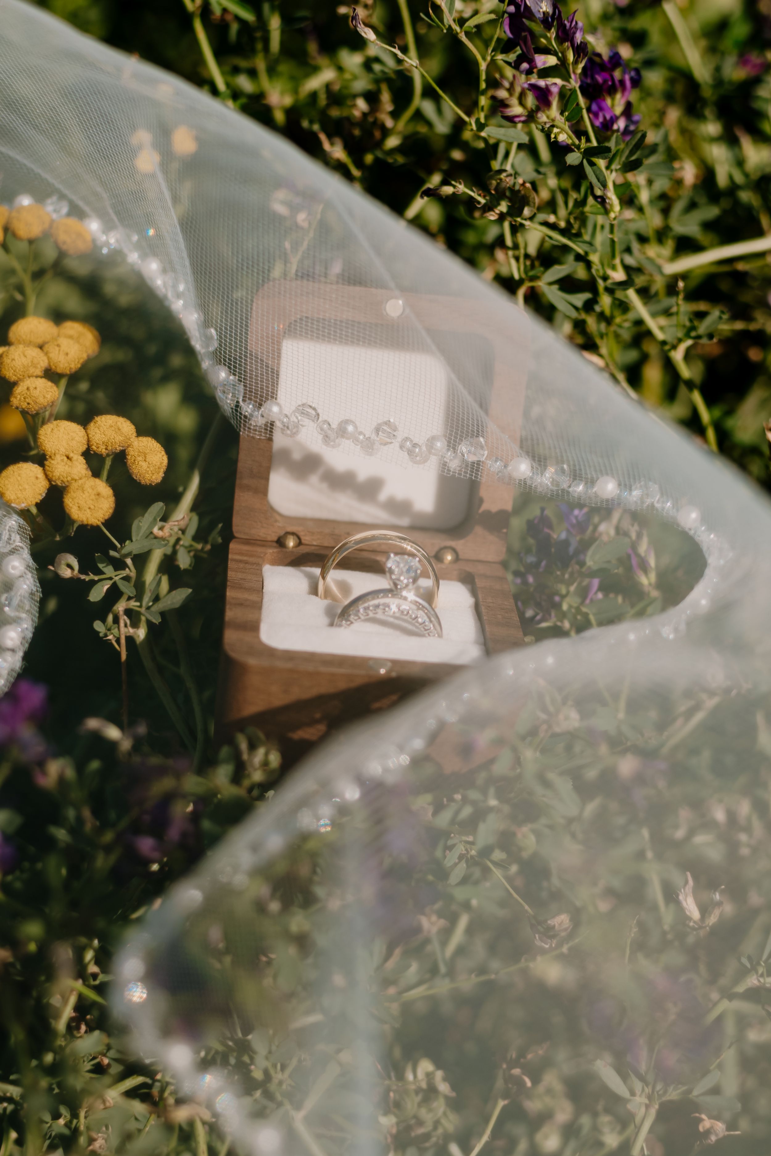 Delicate white tulle veil with floral details draped over wooden elements in an outdoor garden setting.