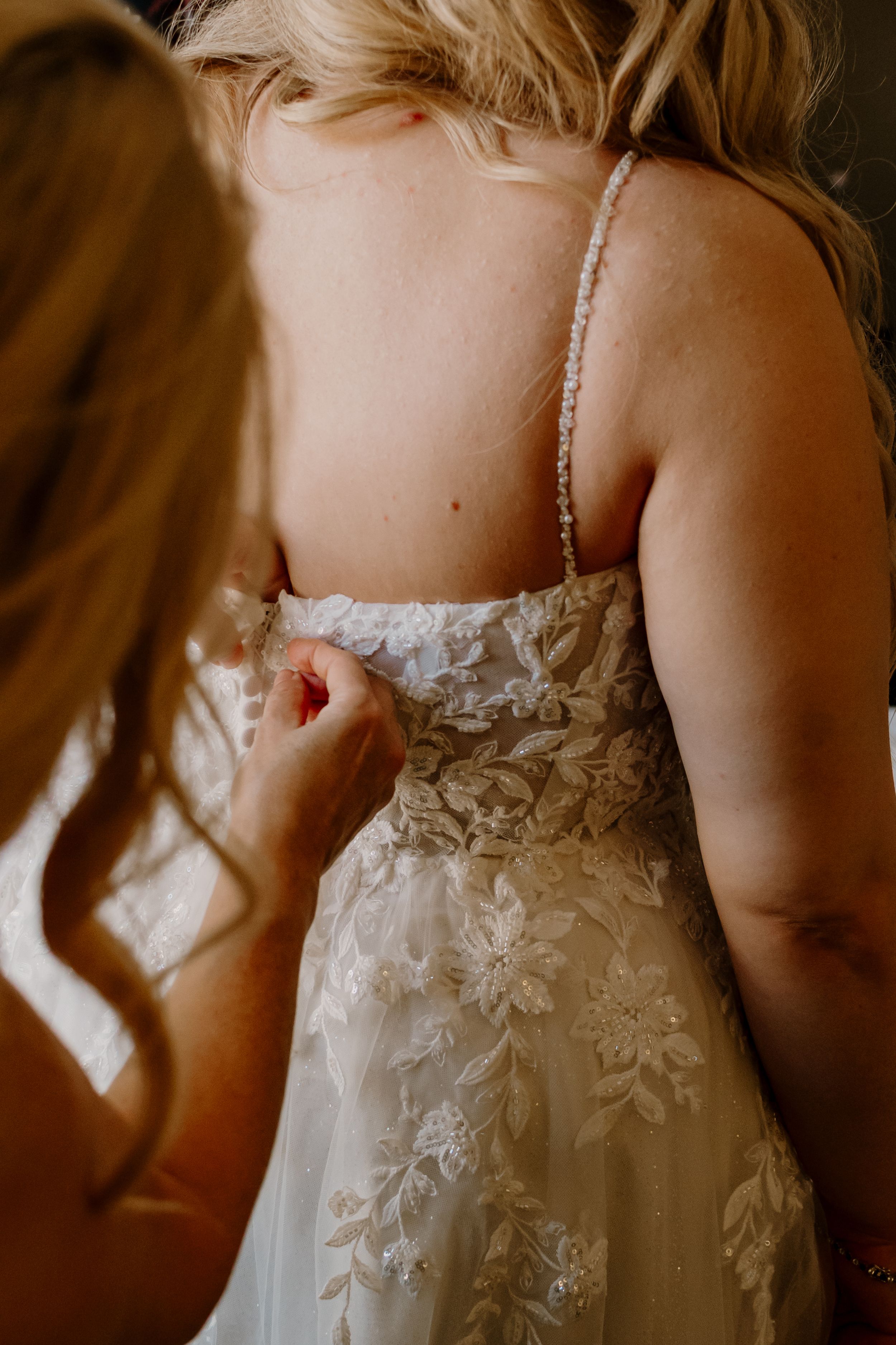 Close-up details of delicate white lace and beading on a wedding dress bodice in warm lighting.