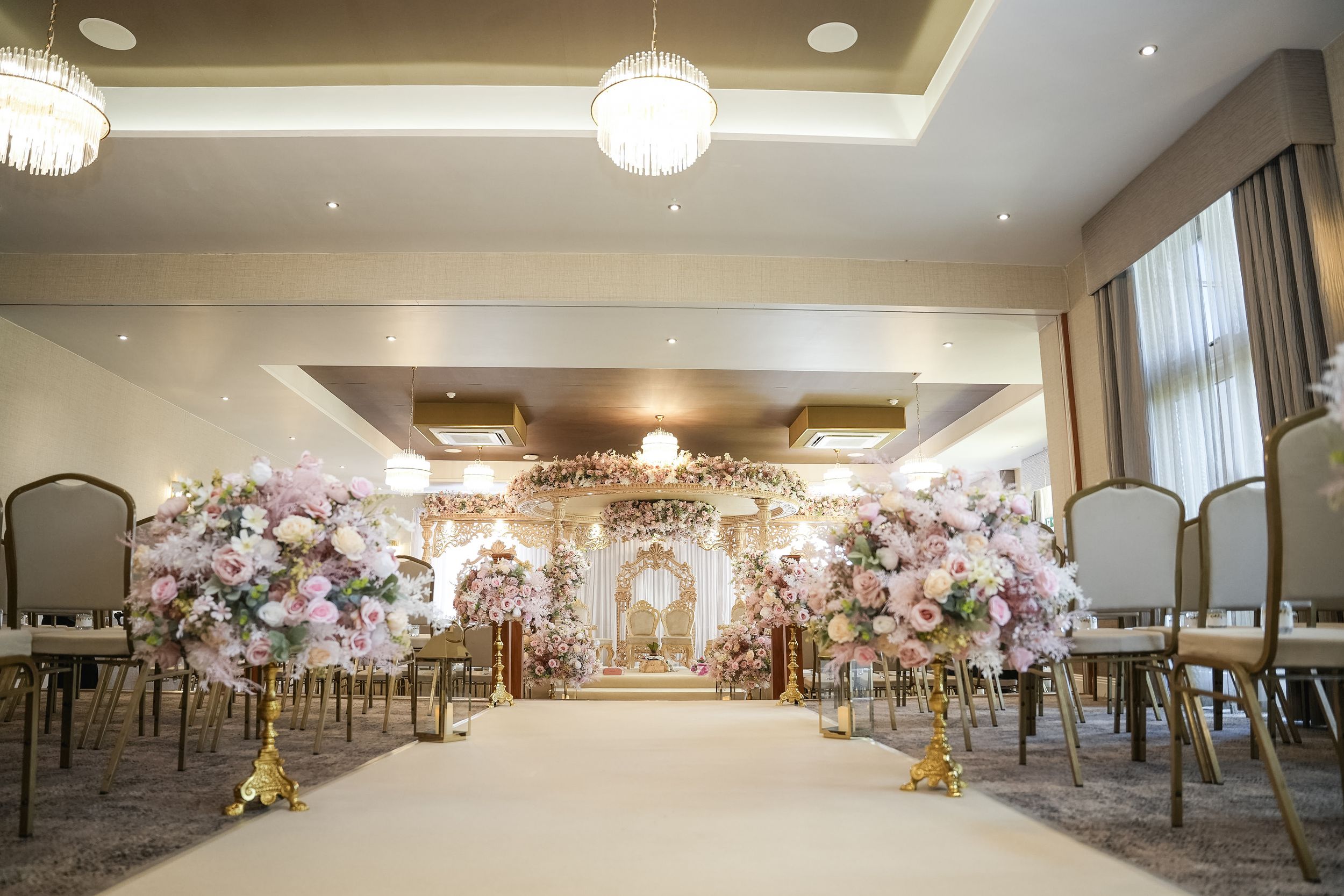 Large elegant banquet hall with round tables, crystal chandeliers, and floral wall decorations for a wedding reception.