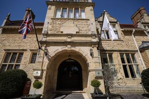 Historic stone building entrance with British flag and arched doorway featuring ornate architectural details and potted plants.