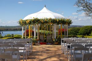 White wedding gazebo overlooking a scenic lake with chairs set up for an outdoor ceremony at sunset.