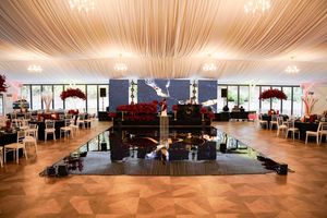 Luxurious ballroom reception venue with dark dance floor, chandeliers and red floral centerpieces.