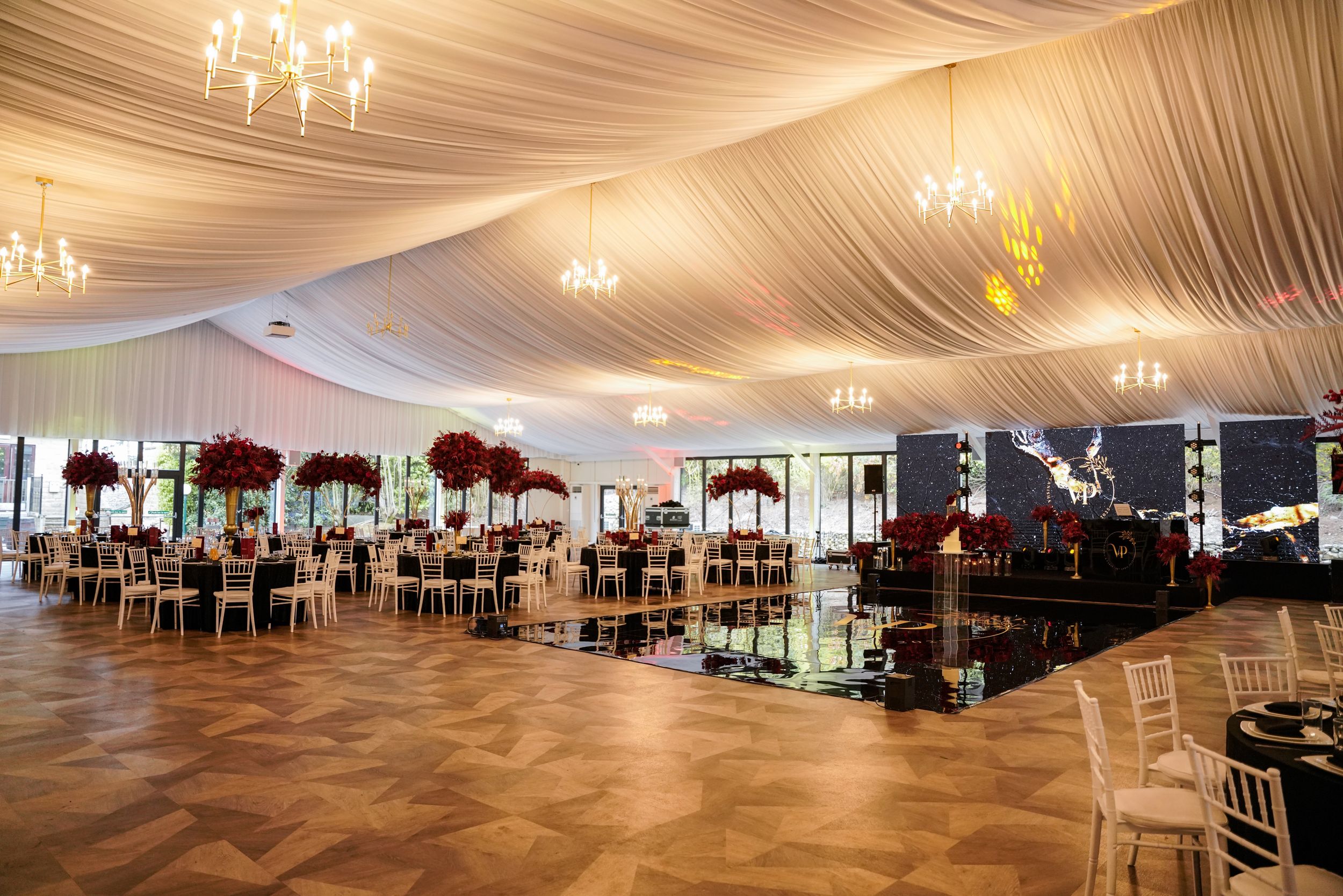 Elegant wedding reception venue with draped white fabric ceiling, chandeliers, and dark wooden chairs.