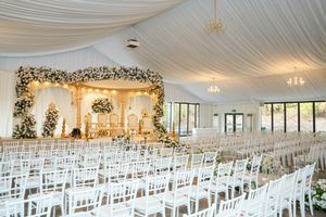 Elegant wedding ceremony setup with white chairs and floral arch altar under draped fabric ceiling with chandeliers.