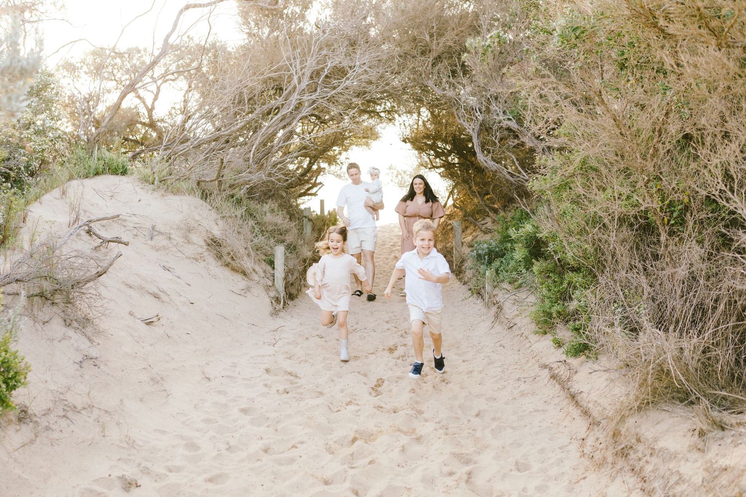 People walking along a sandy coastal path through natural brush and vegetation on a bright sunny day.