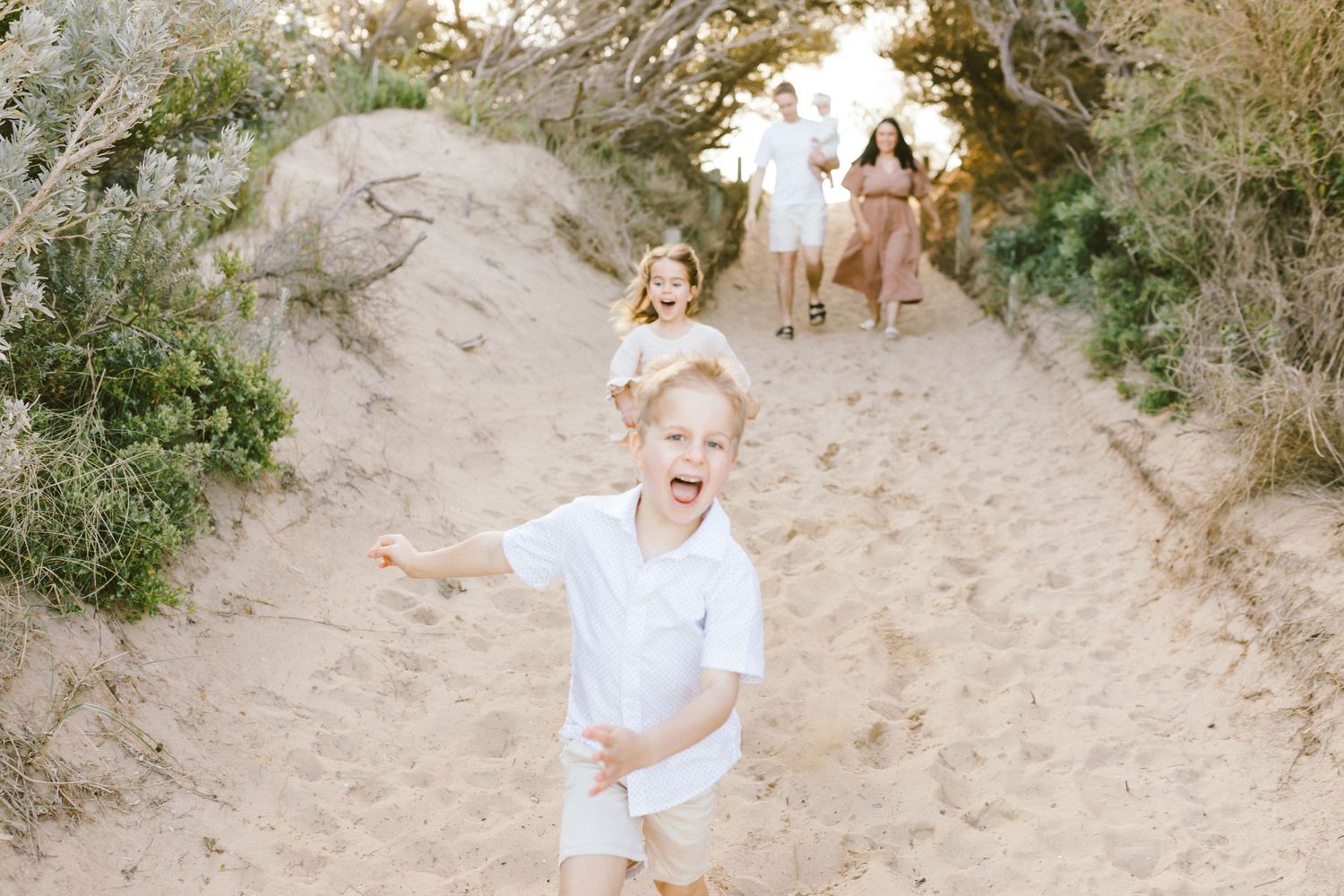 A group of people walking down a sandy path through coastal vegetation on a bright sunny day.