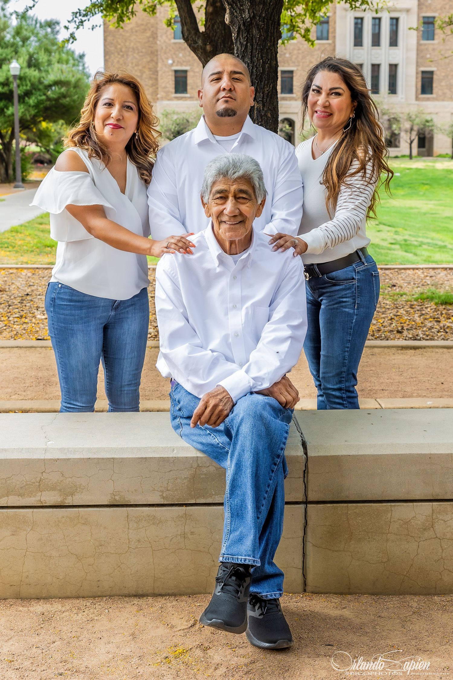 A group in coordinated white tops and blue jeans pose together outdoors on stone steps near a brick building.