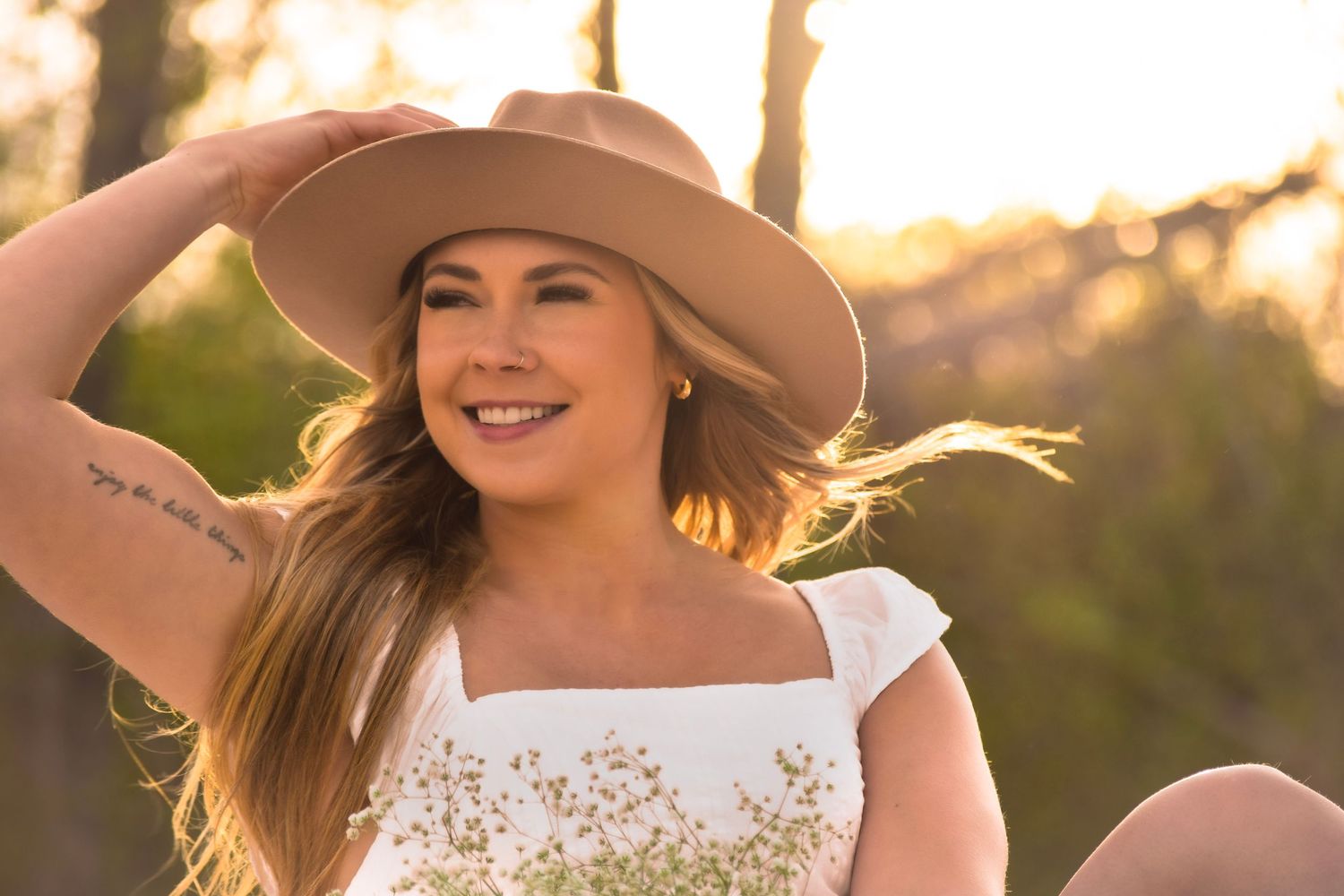Person in a wide-brimmed hat posing outdoors during golden hour.