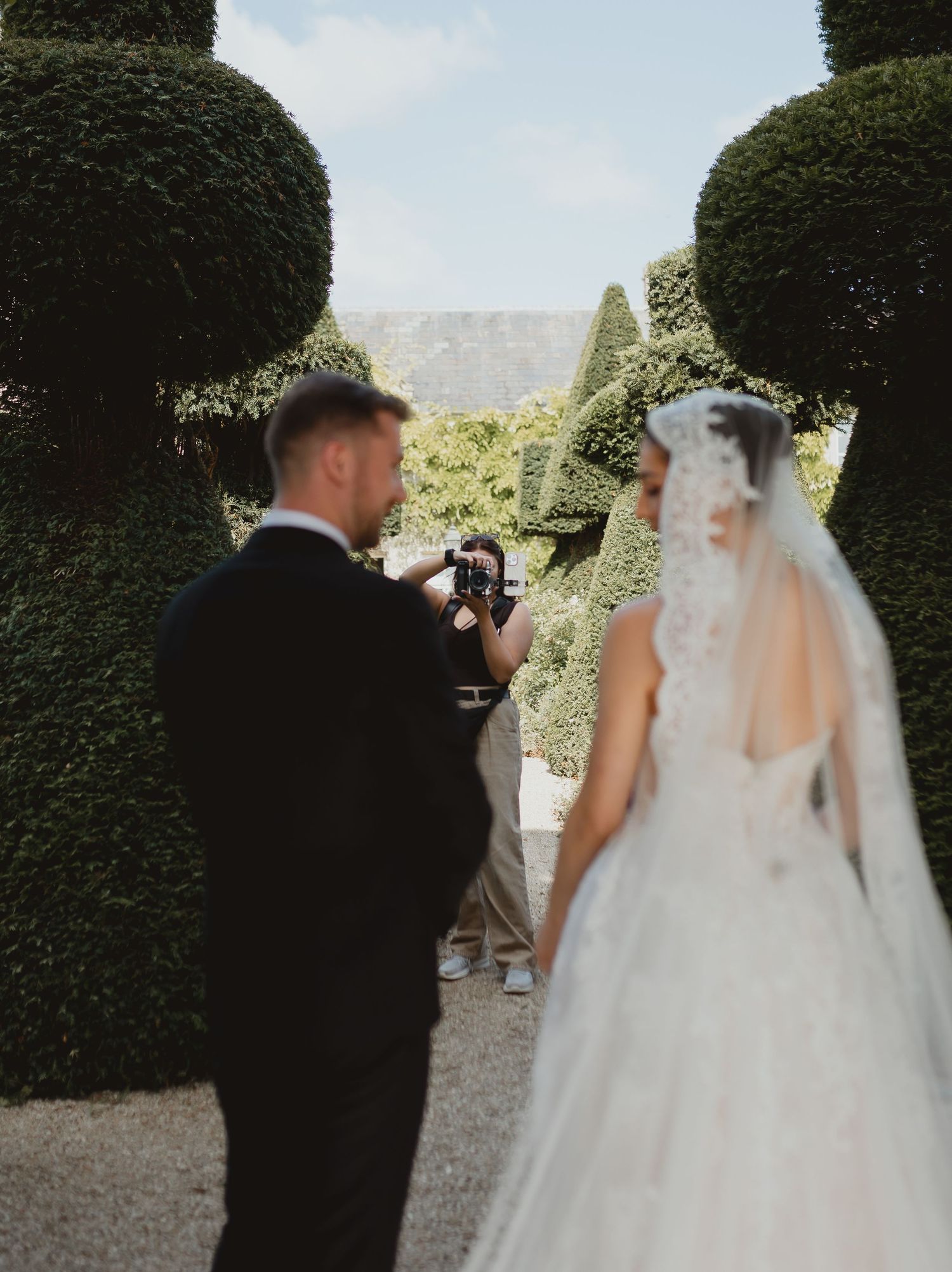 A series of wedding photos showing a couple in formal attire walking together through a garden with manicured hedges.