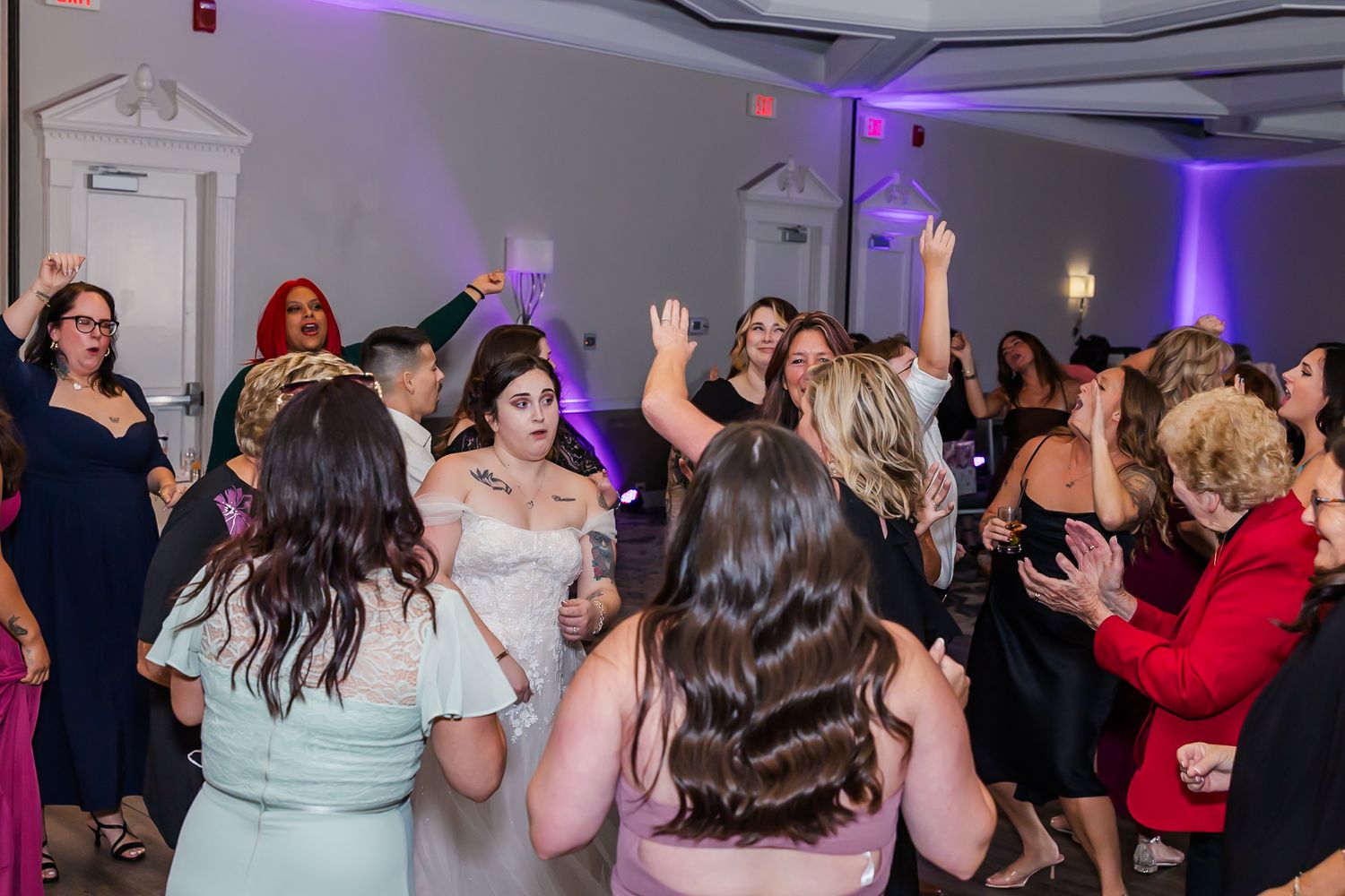 Crowd dancing under purple mood lighting at an indoor celebration event.