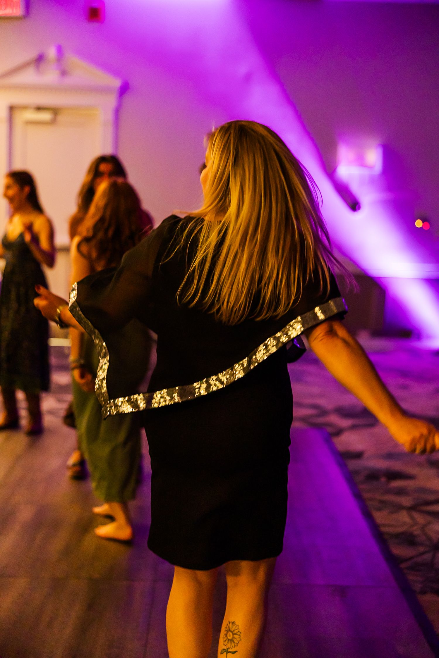 Woman in black dress dancing at a party under dramatic purple lighting.
