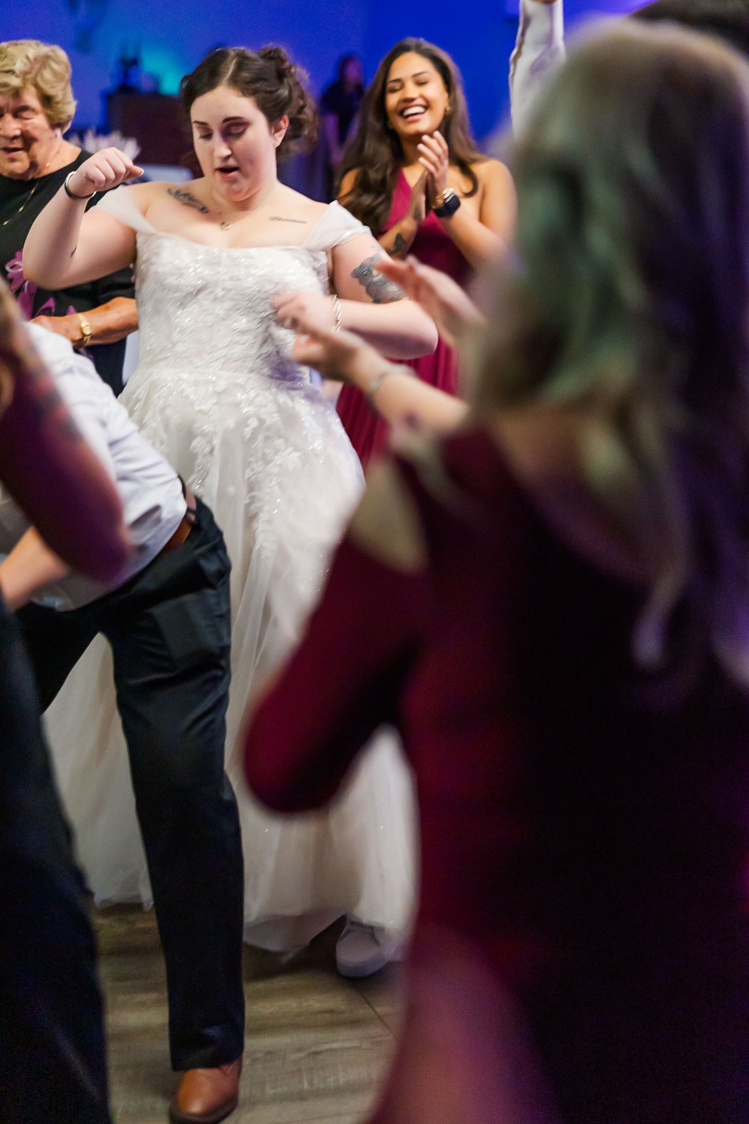 A couple dancing at a wedding reception with the bride wearing a white lace dress and guests visible in the background.