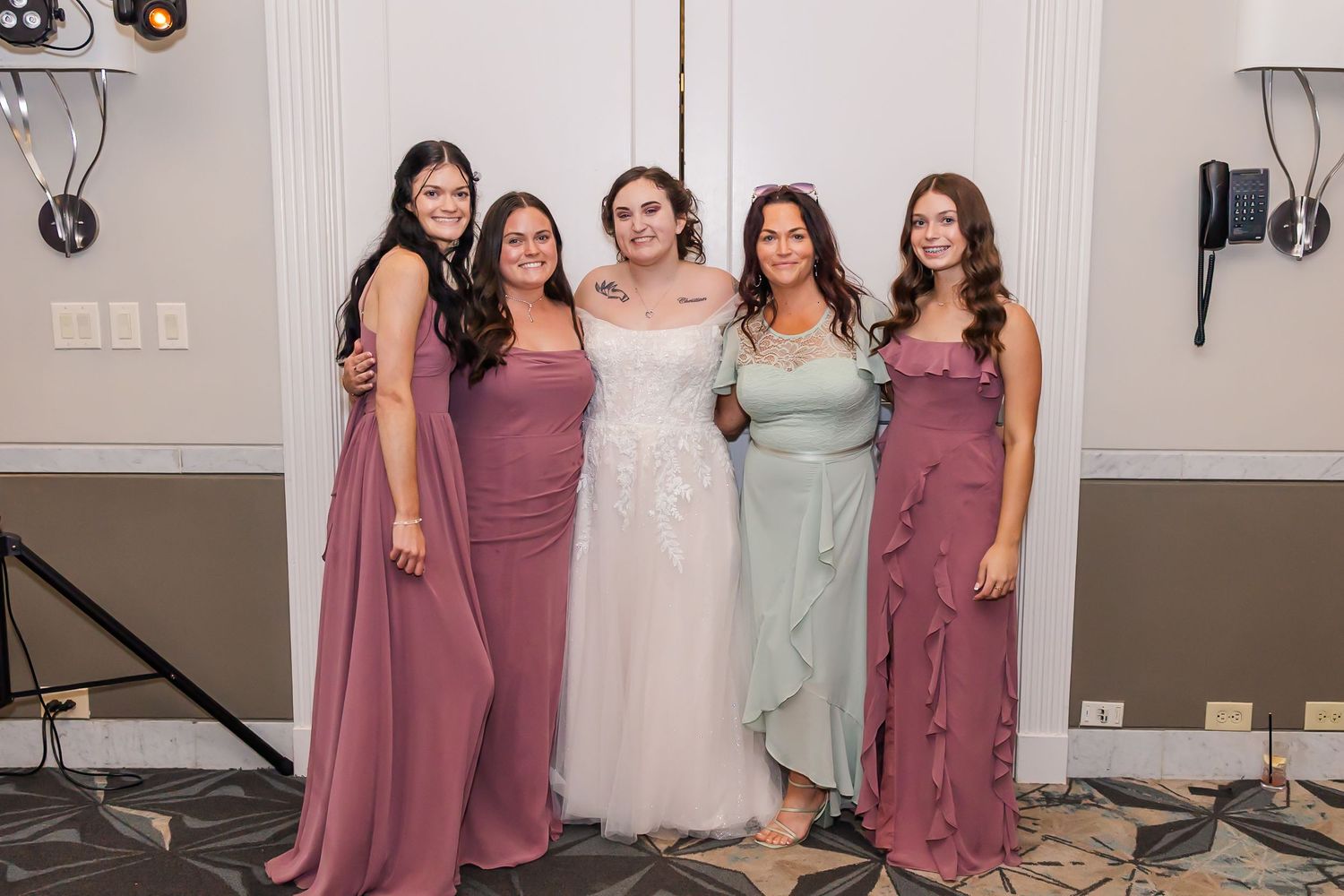 Bridesmaids in mauve dresses pose together with the bride in white for formal wedding photos.