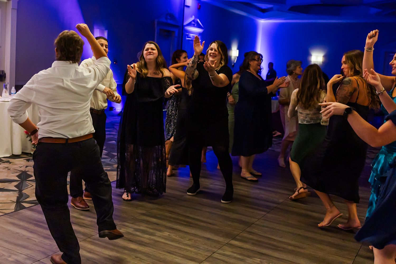 Wedding guests dancing and mingling on a dimly lit dance floor with blue ambient lighting.