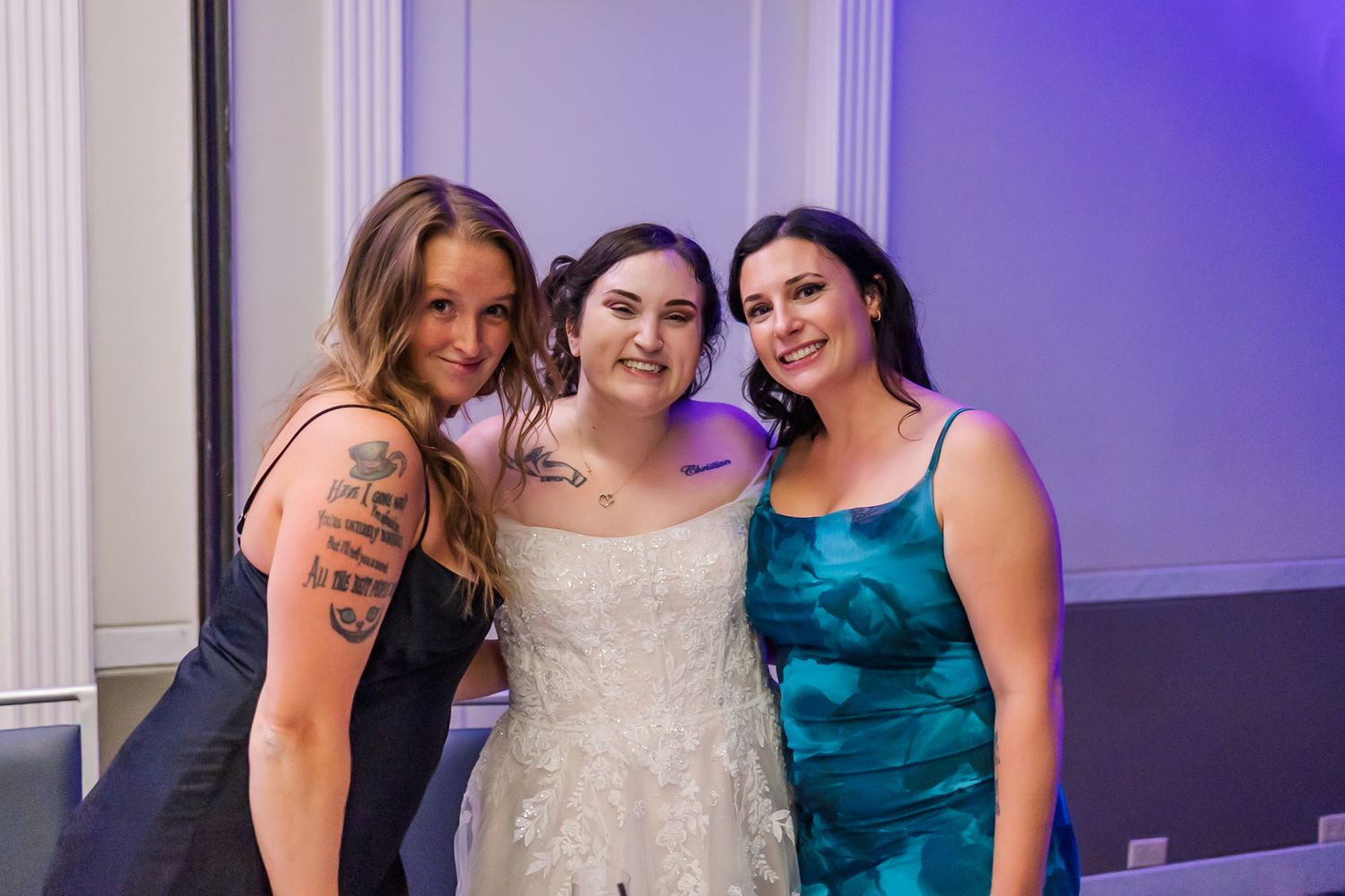 Wedding party members in formal attire pose together in a room with purple lighting and elegant decor.
