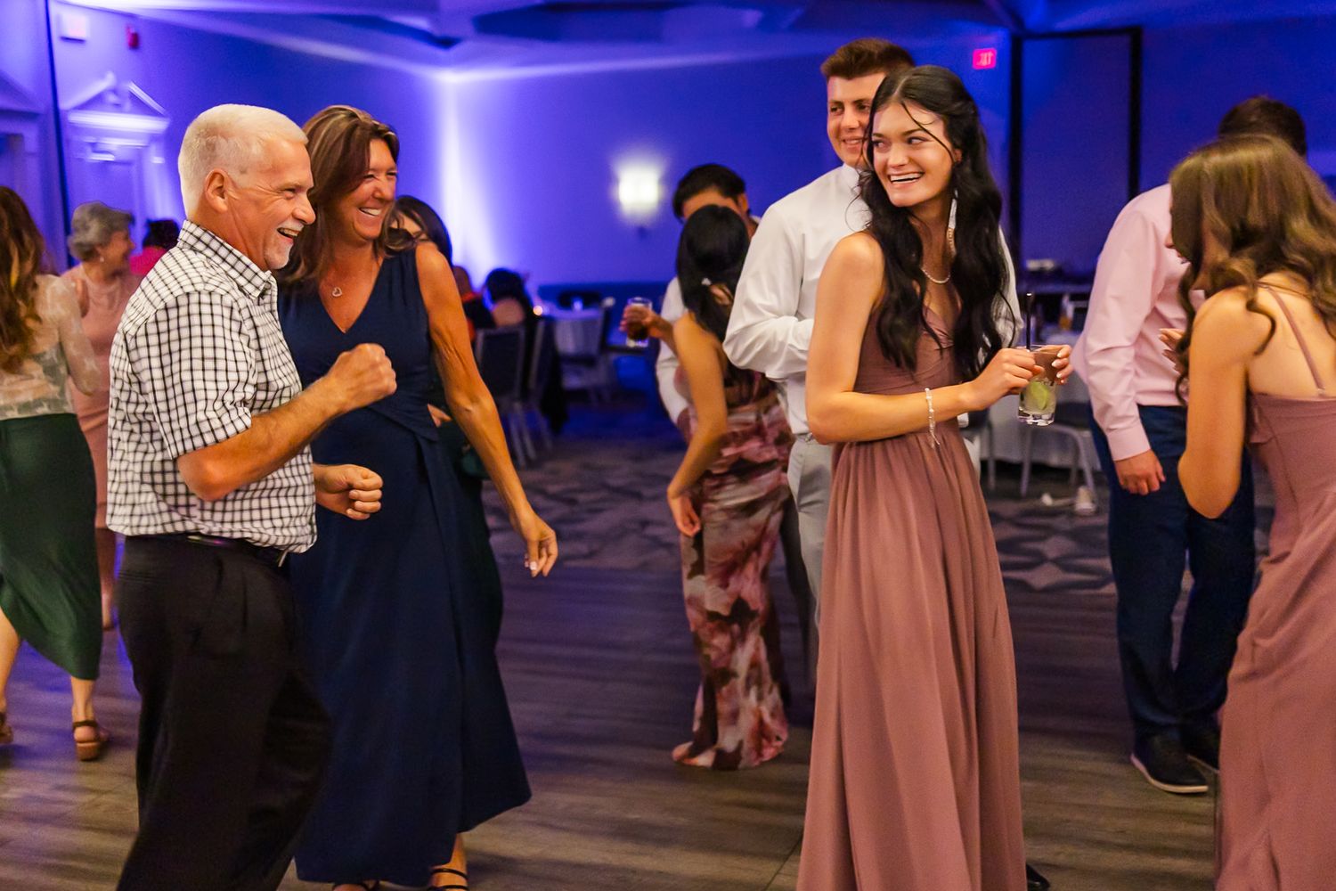 Event attendees dancing and mingling under blue ambient lighting in a reception hall.