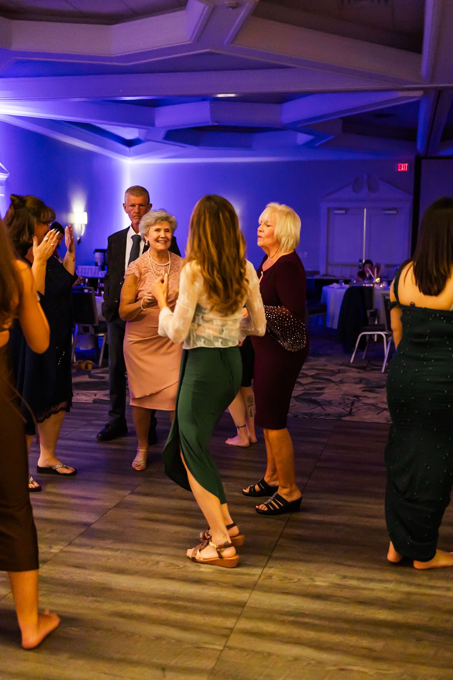 People dancing and socializing at an evening event in a room illuminated with purple and blue lighting.