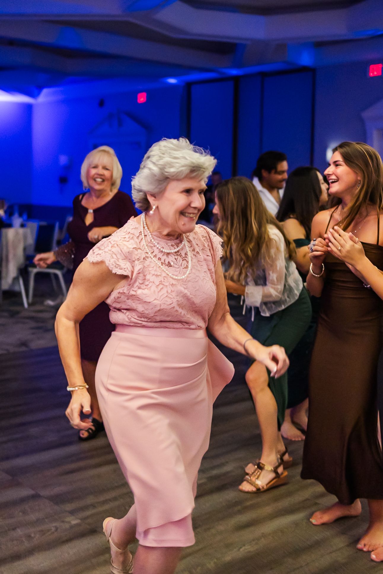 People dancing and celebrating at an event with blue mood lighting in an indoor venue.
