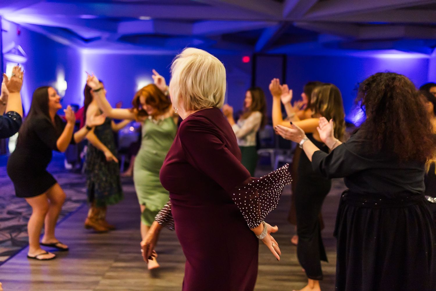 Dancers practice choreography in a spacious studio illuminated by vibrant purple and blue lighting.