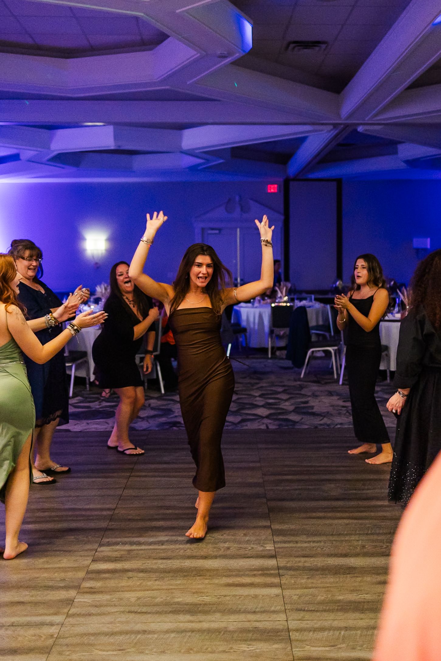 Dance class participants spread across a large studio space with purple ambient lighting and wooden flooring.