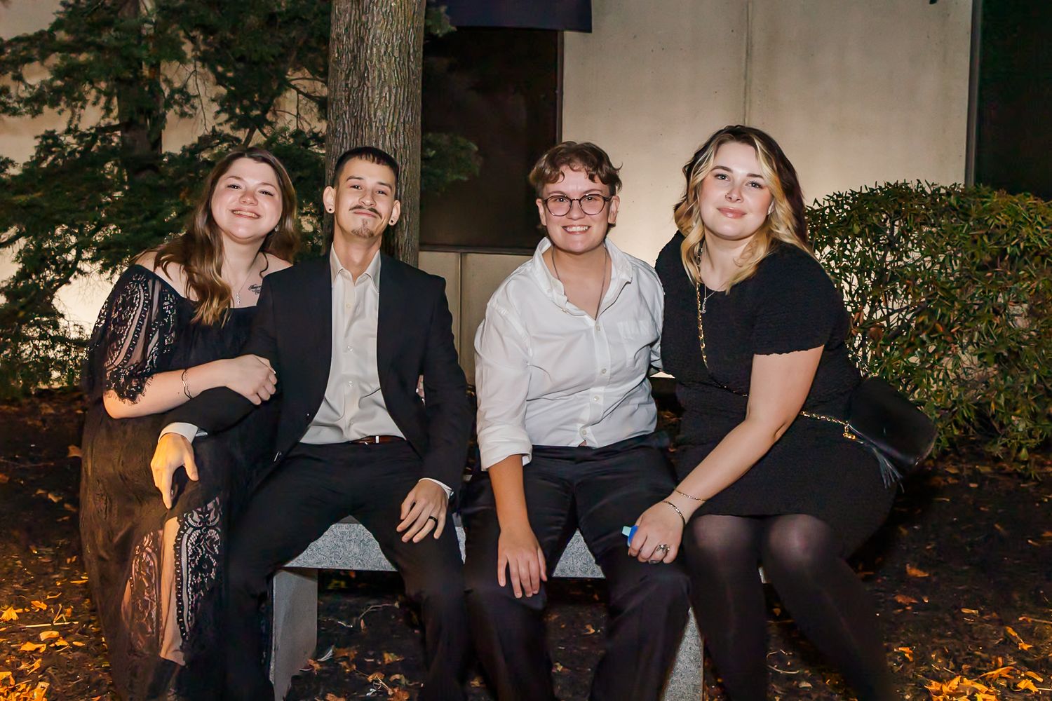 Group sitting together on a bench outdoors at night during a social gathering.