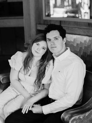 A couple wearing white sits closely together in a romantic black and white portrait photo.