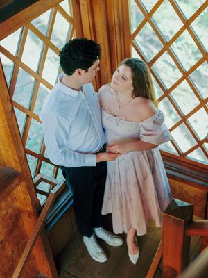 A romantic couple embraces in a wooden-framed sunroom with diamond-patterned windows.