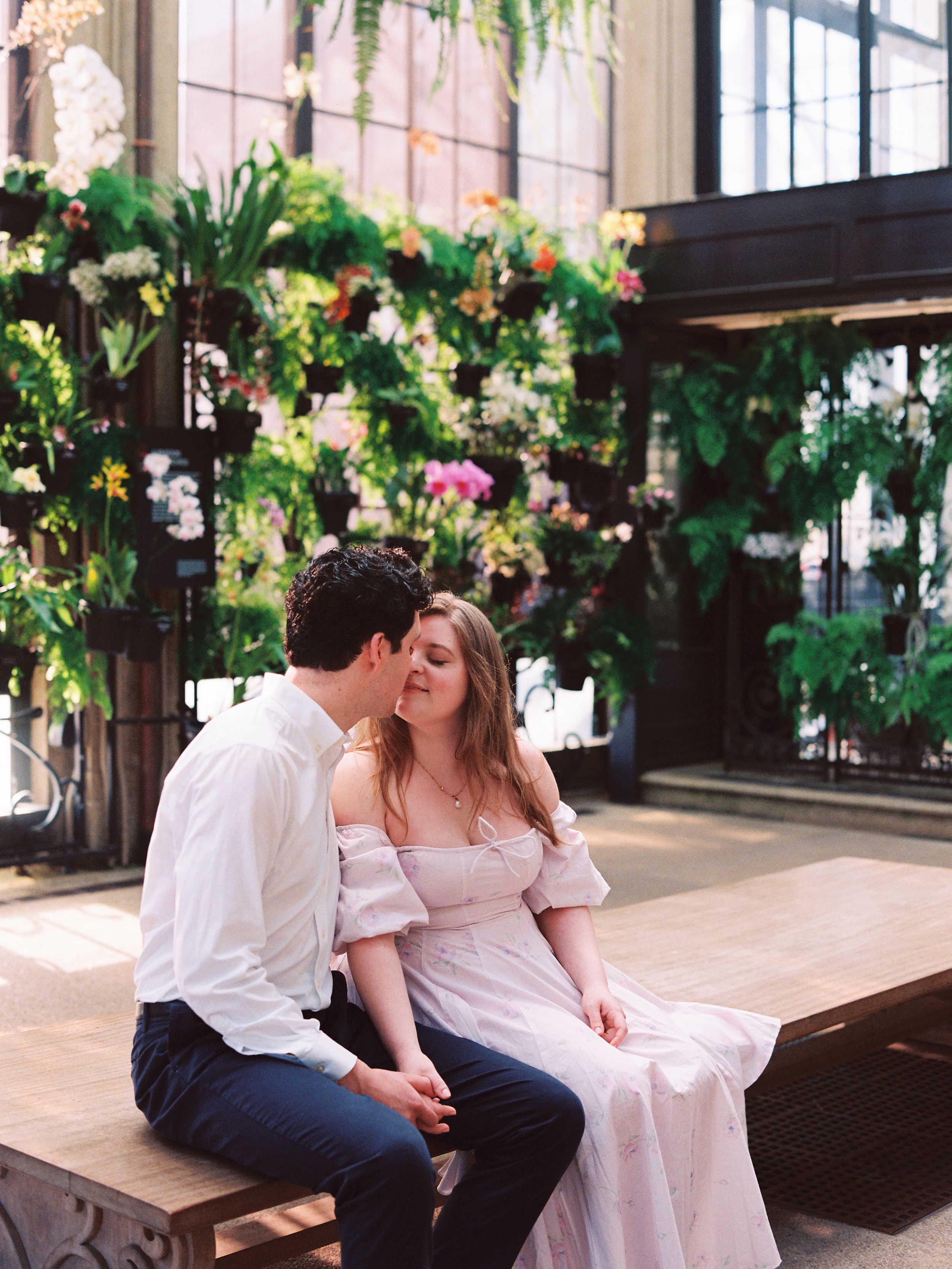 A romantic moment in a greenhouse setting with hanging floral arrangements and natural light streaming in.