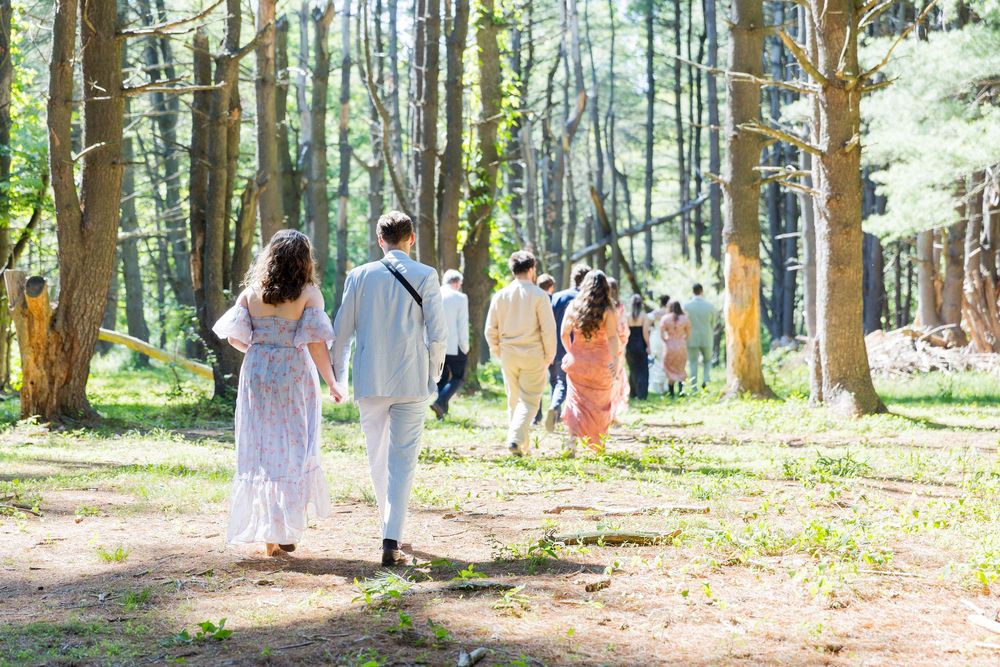 A group of people walk through a sunlit forest path wearing pastel colored clothing on a beautiful spring day.
