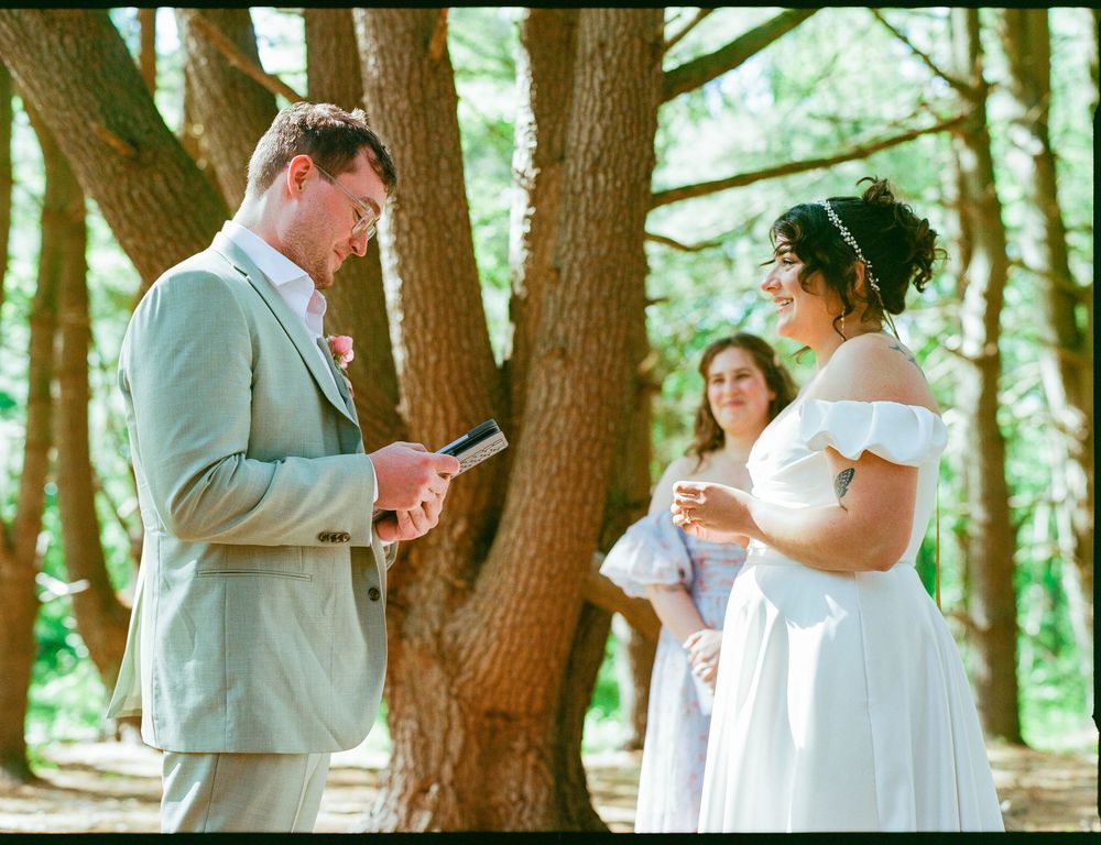 Two people share an intimate moment during a sunlit outdoor garden ceremony while exchanging vows.