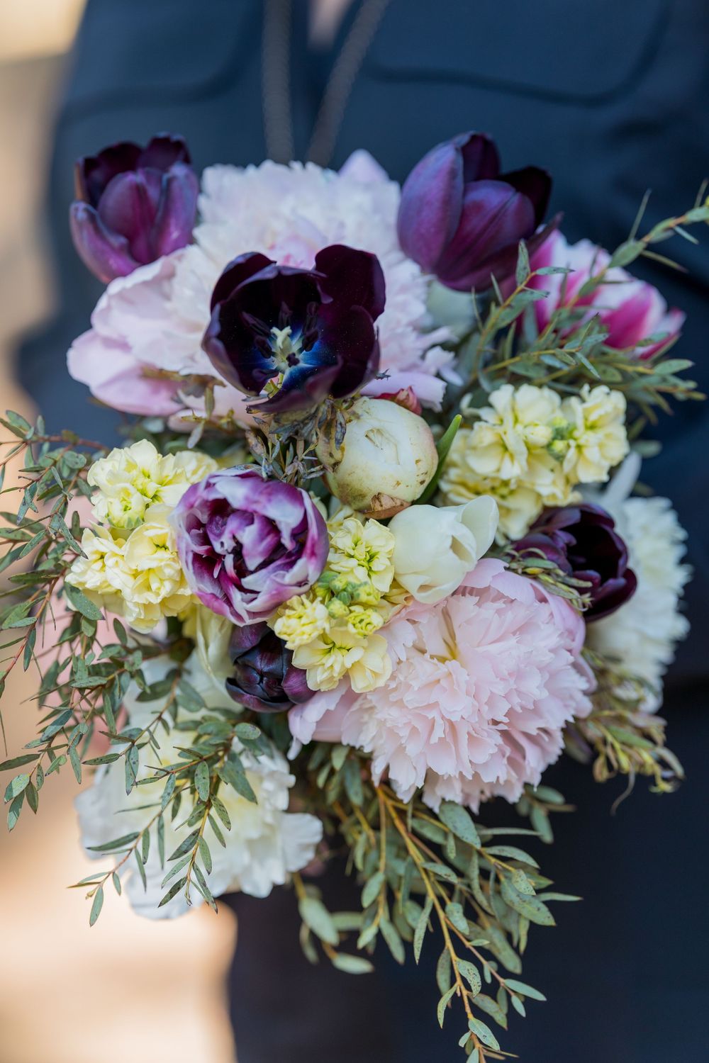 A stunning floral arrangement featuring purple tulips, white carnations, and delicate yellow blooms with greenery.