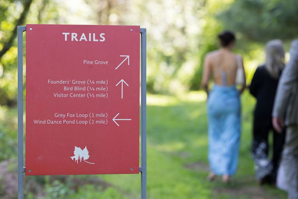 A red trail marker sign against a blurred green background with people walking on a forest path.