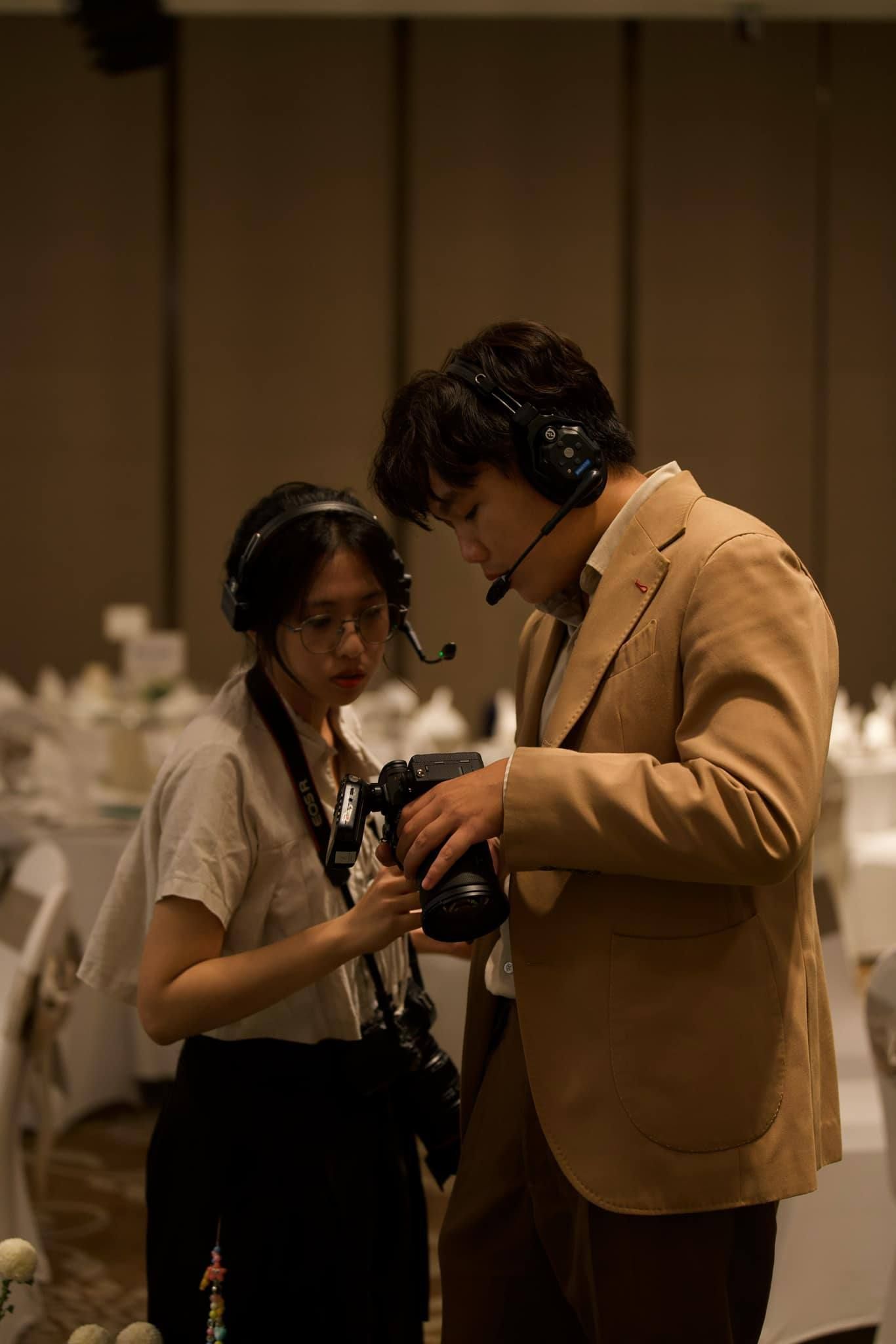 Two photographers wearing headsets review camera shots in a softly lit wedding reception ballroom.