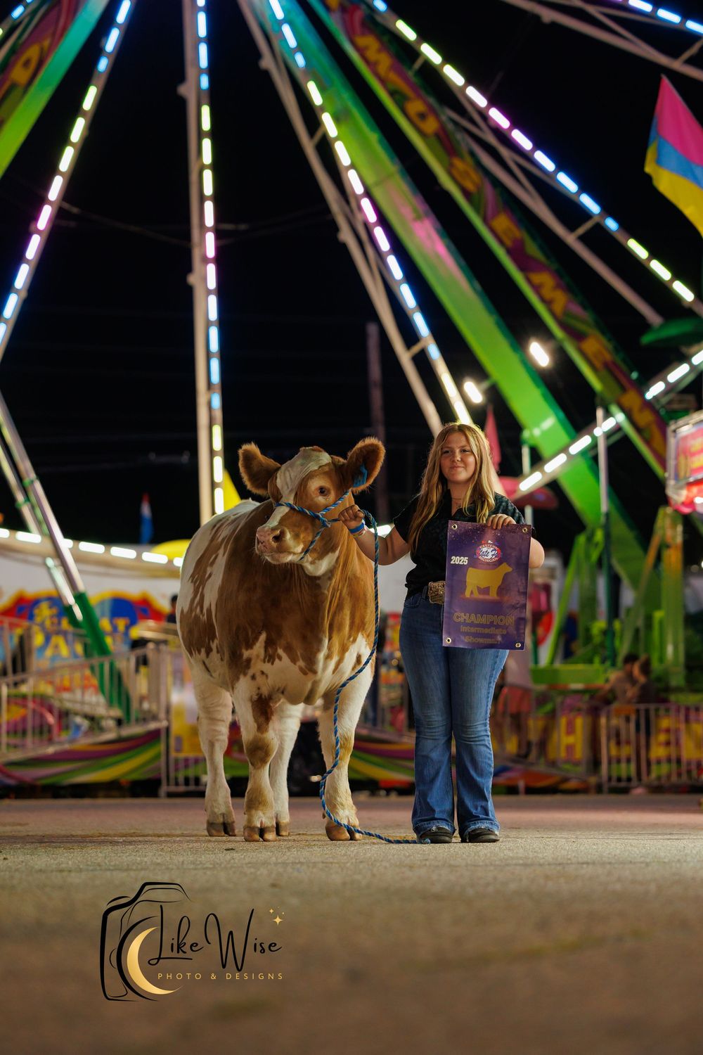 Low-angle view of person and dog standing at carnival with colorful lights of rides glowing in background at night.
