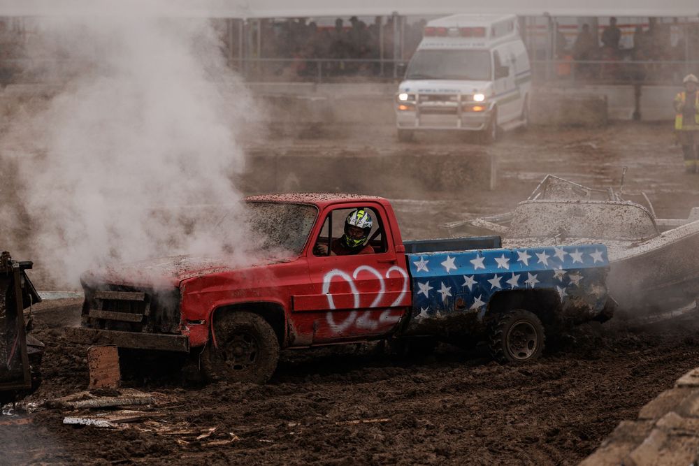 Monster trucks kick up dirt and dust while performing stunts at an outdoor motorsports event.