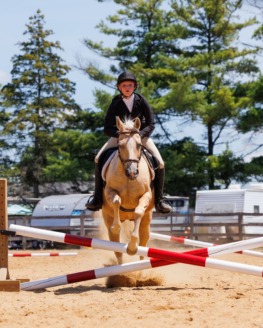 Sequence showing a horse and rider jumping over progressively higher red and white poles in a sandy outdoor arena.