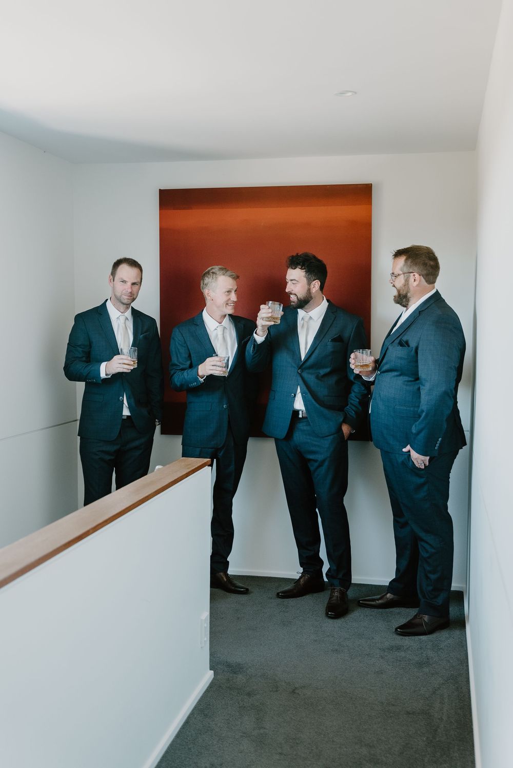 A group of wedding party members in dark suits socializing together in a modern indoor space.
