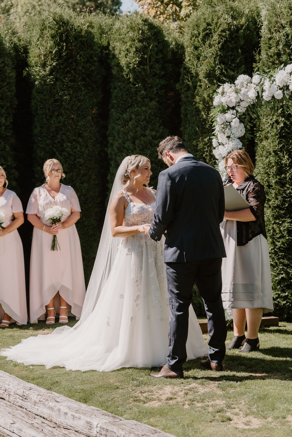 Wedding party poses for casual outdoor photos in front of lush green hedges.