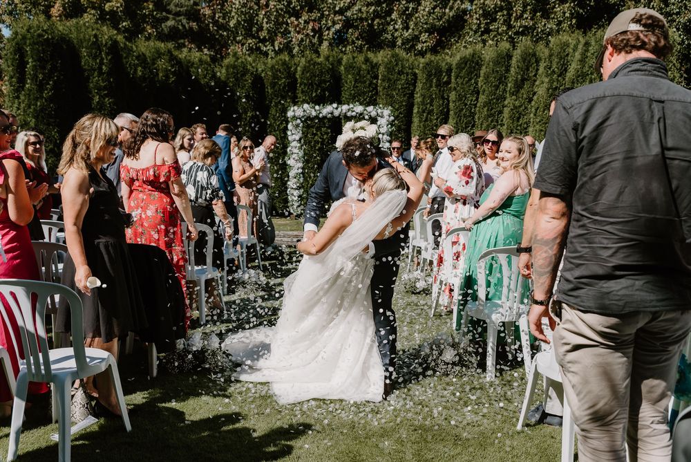 Wedding ceremony guests celebrate as confetti falls in an outdoor garden setting.