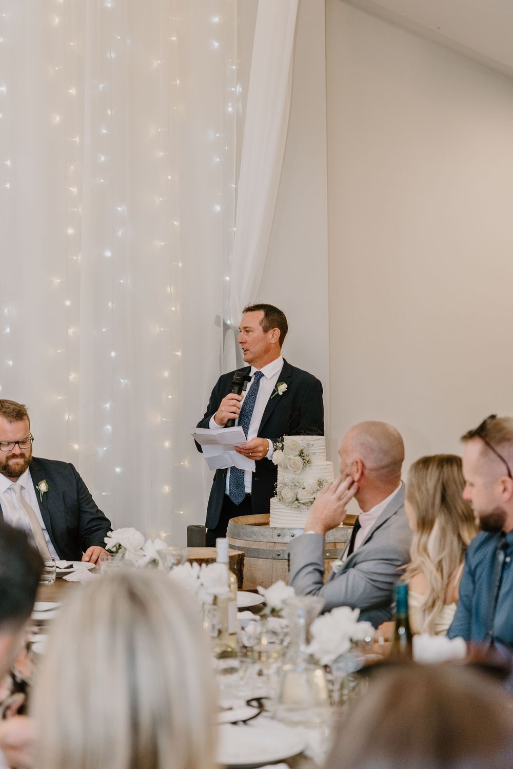 Wedding reception venue decorated with twinkling string lights and white drapes during dinner speeches.