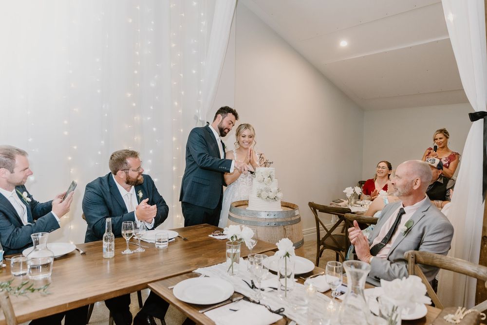 Guests laughing and clapping during a wedding speech at an elegant reception dinner with white table settings.