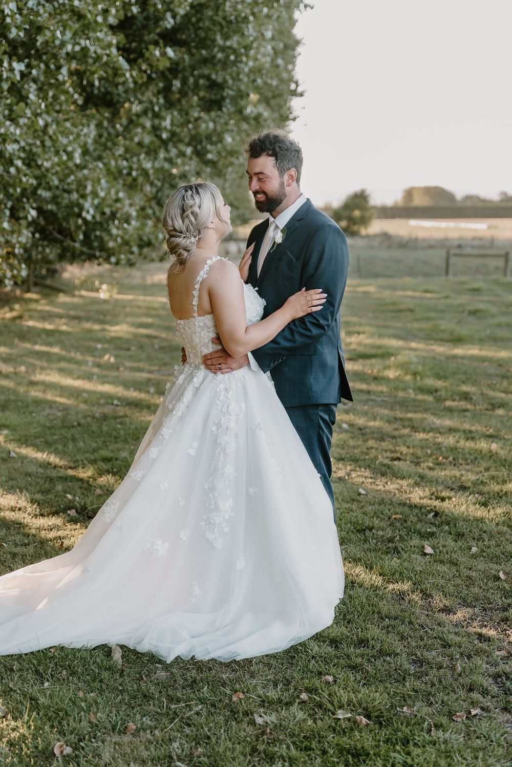 Newlyweds share an intimate moment outdoors in elegant wedding attire during golden hour.