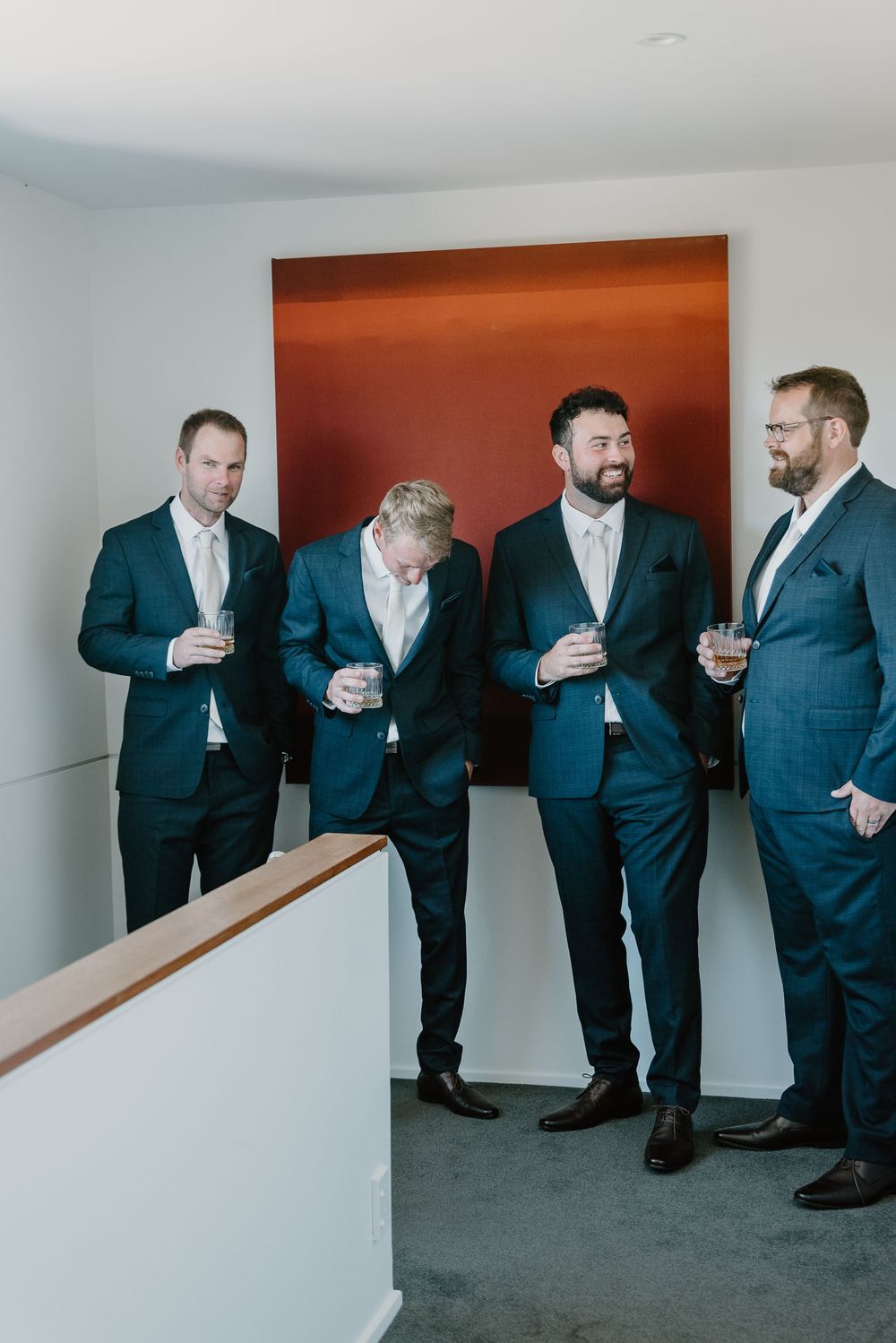 Groomsmen in navy suits share a lighthearted moment in a minimalist hallway before the wedding ceremony.