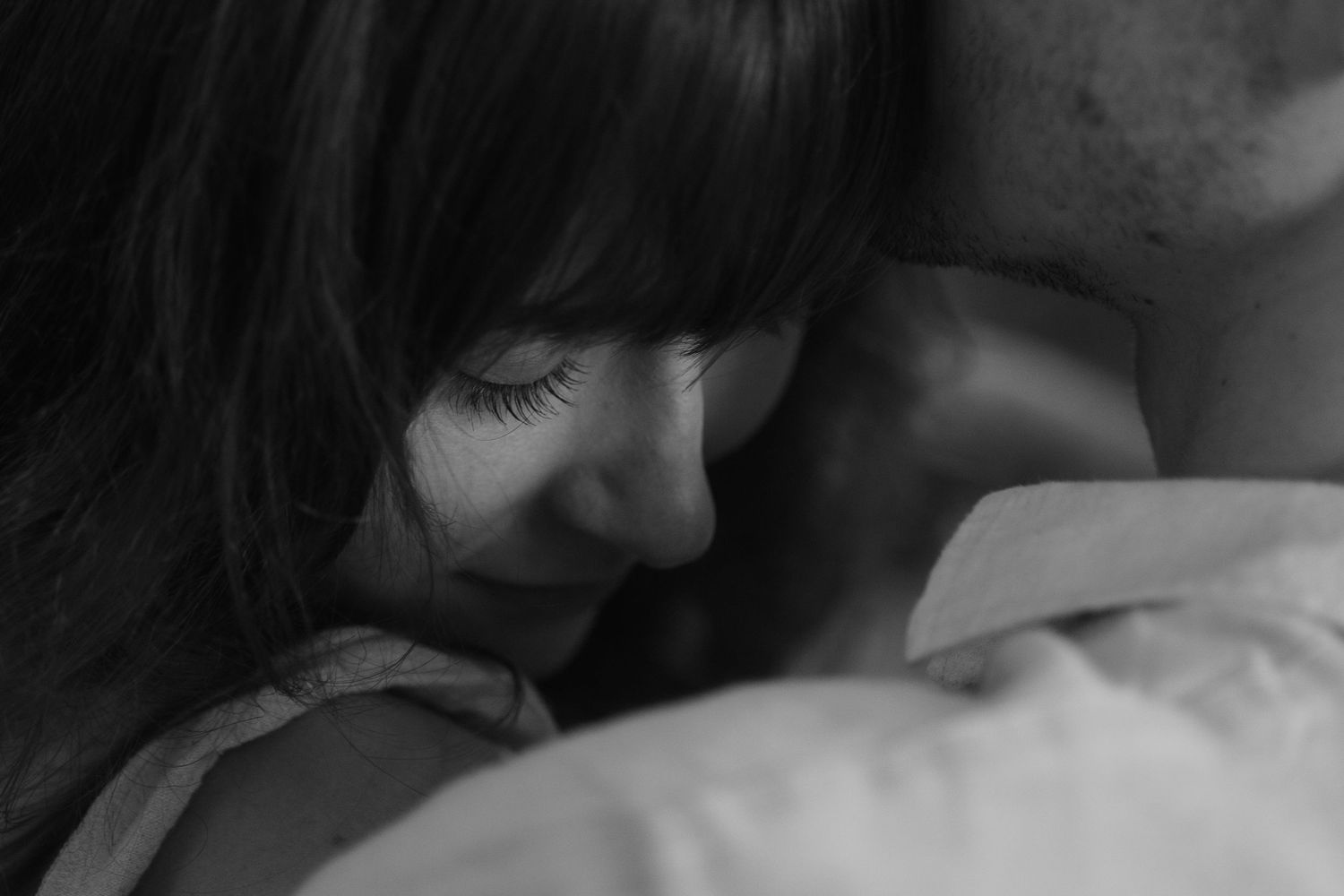 A close-up black and white profile portrait showing someone smiling warmly while resting on a pillow.