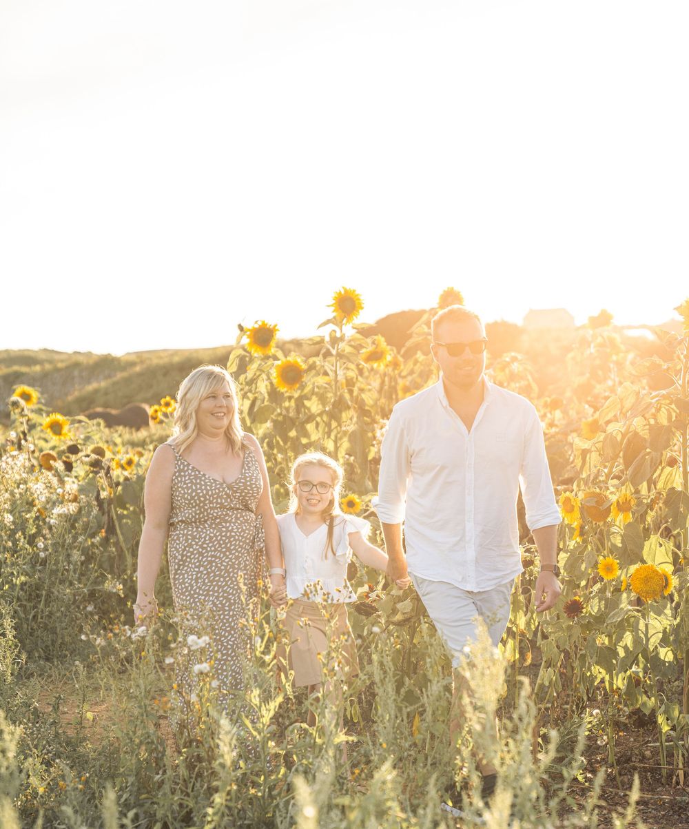 A family walks together through a sunlit field of tall wildflowers during golden hour.