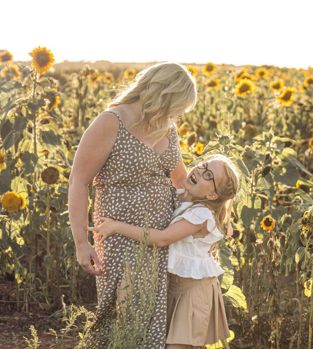 A parent and child share a tender moment in a backlit sunflower field at golden hour.