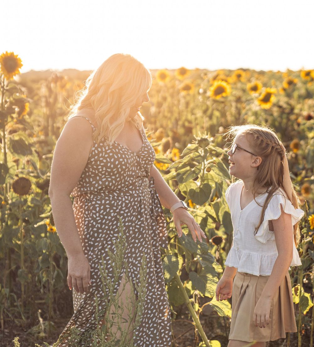 Two people chat in a sunlit field of sunflowers at golden hour.